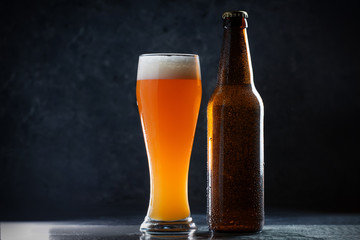 Glass of cold unfiltered wheat beer and a beer bottle on a bar with copy space
