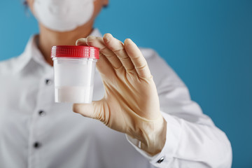 A doctor's gloved hand holding a bottle of a container with a sperm sample for medical analysis.
