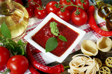 Tomato paste with basil leaves,fresh tomatoes, olive oil,pasta, red peppers on a wooden boardon
