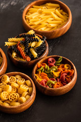 Fototapeta na wymiar selective focus of various raw Italian pasta in wooden bowls on black background