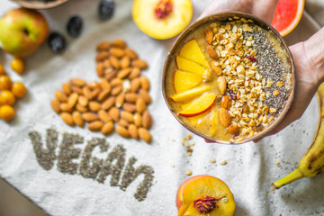 
Making a vegan smoothie bowl with peach, banana, chia, granola and almonds in a coconut bowl. Vegan breakfast.  Almond heart