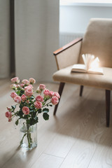 Modern room interior with armchair, book and fresh roses on table. Interior of beautiful living room decorated with flowers