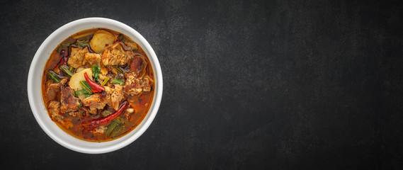 Tom Yum, Thai food, hot, spicy and sour stewed beef soup in bowl on dark gray, grey, black tone texture background with copy space for text, 64 x 27 ultra widescreen aspect ratio