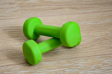 Close-up of a pair of bright green little female dumbbells on the wooden floor. Fitness concept, sport, body building.Concept healthy lifestyle, sport and diet. Sport equipment. Copy space