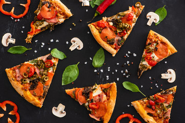 top view of delicious Italian pizza slices with vegetables and salami on black background