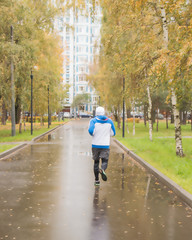 A young athlete runs through the Park on a rainy autumn day. sports in the open, from behind