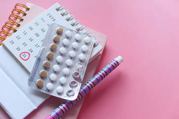 birth control pills , calendar and notepad on pink background 