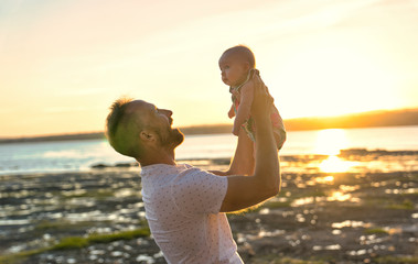 father and baby child girl at the sunset on the waterscape