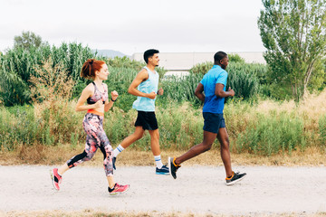 Three friends exercising outdoors, running in rural setting