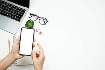 Flat lay, Workspace business office and education concept on white table desk with hand holding blank screen phone and laptop computer, Top view  with copy space