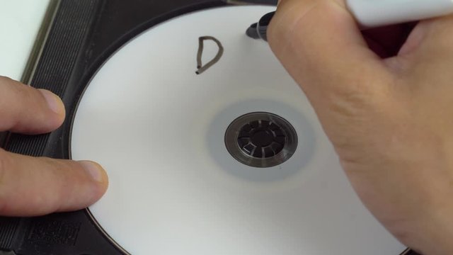 a human hand writes data on a white CD. Marker. Marks that important information is saved on this disk.