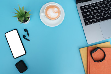 Workspace back to school and education concept on blue table desk background with laptop computer, blank screen phone and stack of book, earphone, green plant and coffee cup, flat lay with copy space