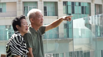Asian senior elder couple on skyscraper rooftop looking over Bangkok skyline - Powered by Adobe