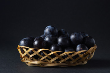 Plum in a wicker basket. Photo on a black background. Summer harvest