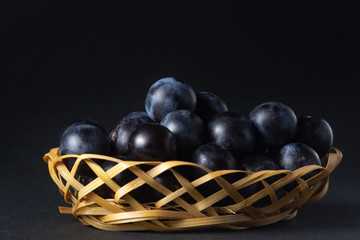 Plum in a wicker basket. Photo on a black background. Summer harvest