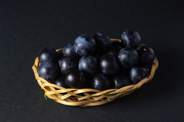 Plum in a wicker basket. Photo on a black background. Summer harvest