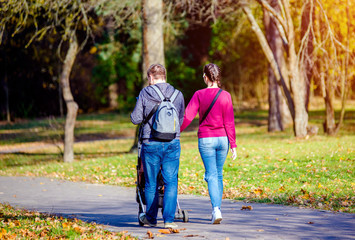 Fototapeta premium A married couple rolls a baby stroller in a city Park 