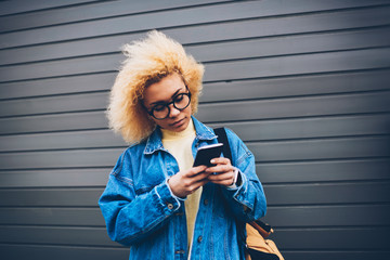 Pretty hipster girl checking smartphone notification standing on wall promotional background,...