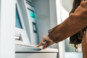 Close up shot of young adult woman's hand. He typing pin code on keypad of ATM machine while using...
