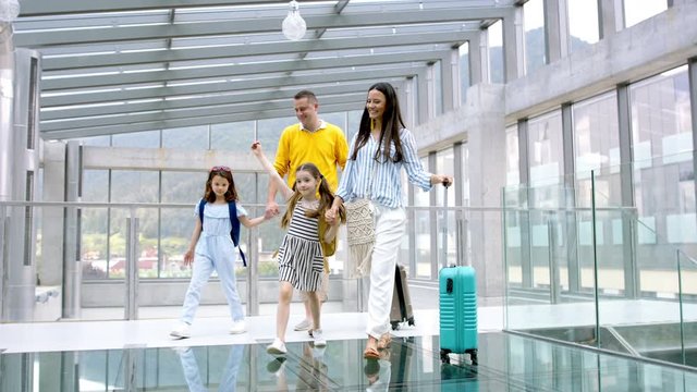 Family with two children going on holiday, walking at the airport with luggage.