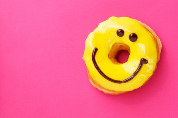 Yellow round donut with smile on pink background. Flat lay. Copy space..