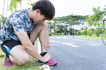 Asian man use hands hold on his ankle while running on road in the park. Injury from workout...