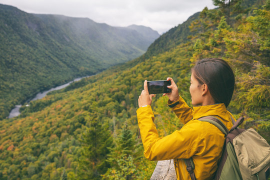 Hike woman hiker taking picture with phone of river view from top of trail hiking in Parc National de la Jacques Cartier, Quebec, Canada autumn travel camping lifestyle.