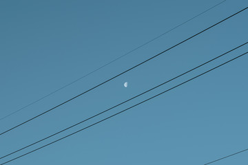 The moon with voltage wires and blue sky