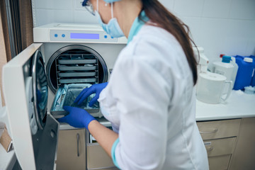 Doctor assistant in blue gloves sterilize dental steel set tools in autoclave