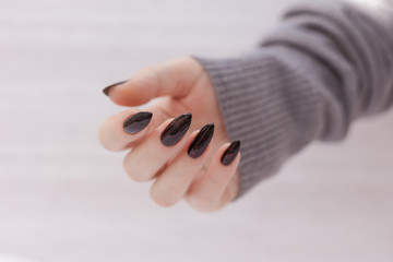 Female hand with long nails and gray black manicure with bottles of nail polish
