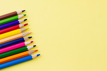 Colored saturated pencils for drawing on a yellow background. Place for your text. View from above. Education concept.