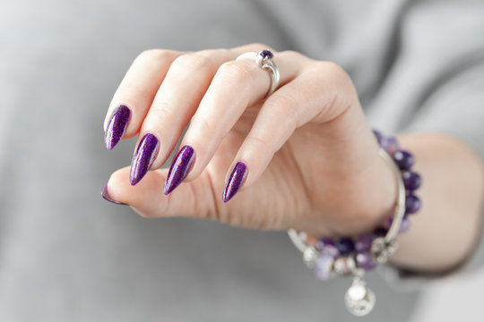 Female hand with purple violet long nails and nail polish bottle