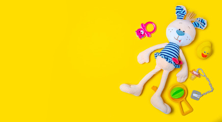 Soft toy hare rabbit, rattles, baby soother on yellow background, top view