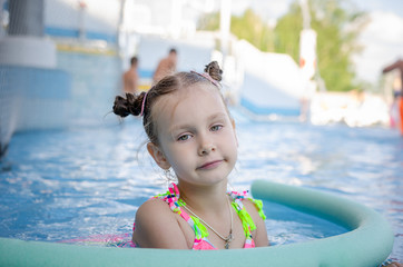 little beautiful girl swimming with a foam noodle in a outdoor pool. summer vacation in the water...