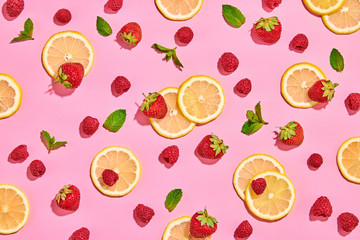 Red raspberry, strawberry, lemon colorful pattern on pink background. Fresh berry closeup, strawberry wallpaper, top view. Lemonade creative concept, fashionable trendy summer beverage, flat lay