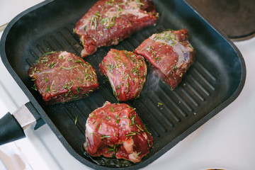 Four raw steaks are fried on a grilled pan.