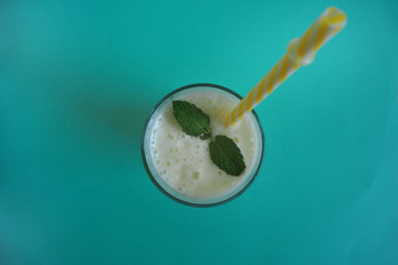milk banana cocktail with a sprig of mint in a glass with a yellow tube top view on a turquoise background