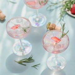 Summer drink with white sparkling wine. Homemade refreshing fruit cocktail or punch with champagne, strawberries, ice cubes and rosemary on light blue background.