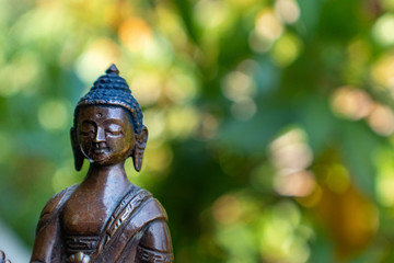 Small metal buddha figurine with dappled sunlight and green background