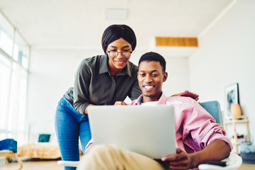 Cheerful african american couple enjoying making shopping together in web store using laptop computer at home, young dark skinned marriage watching video on netbook connected to wireless internet