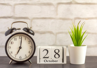 October 28 on a wooden calendar next to an alarm clock on a dark table .One day of the autumn month.Calendar for October. Autumn