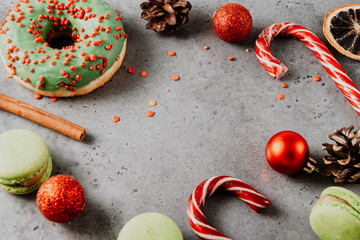 lollipops, cone, cinnamon stick, green doughnut, cookies, macaroon, red Christmas balls on a gray background,