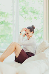 Happy young beautiful woman is sitting on couch talking on phone and laughing