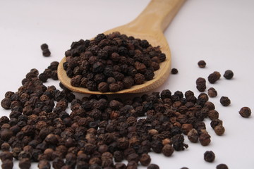 Black pepper in wooden spoon isolated on white background