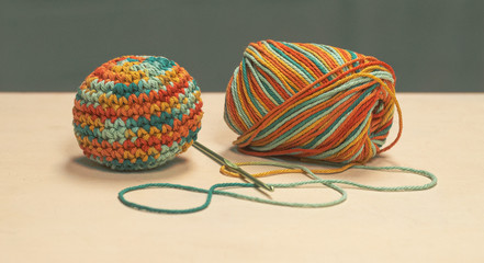 Skein of multi colored cotton yarn with a crochet hook and a completed amigurumi ball