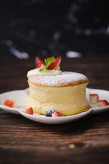 Fluffy souffle pancakes with cream and berries on white plate set on wooden table.