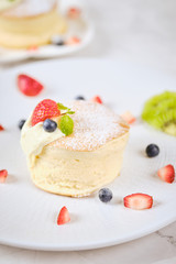 Fluffy souffle pancakes with cream and berries on white plate set on cafe table.
