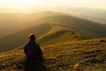 Alone tourist on the edge of the mountain hill against the backdrop of an incredible sunset mountains landscape