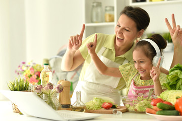 Cute little girl with her mother cooking together at kitchen table