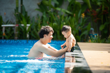 Fototapeta na wymiar Asian father playing with his little son in pool. Asia people swim in pool outdoor.